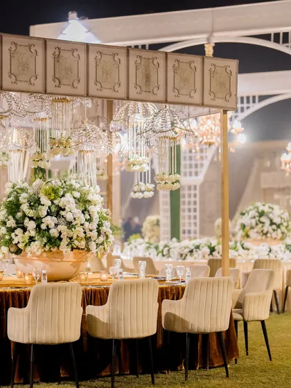 An elegant outdoor cocktail reception setup, with hanging crystal chandeliers, plush seating, and beautiful floral arrangements.