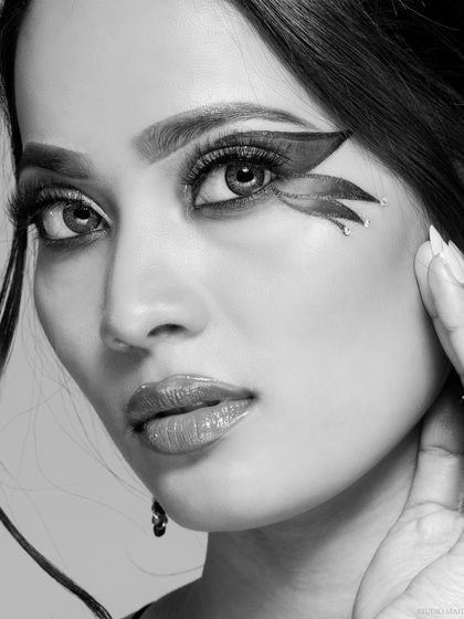 The black and white version of the graphic eyeliner look, creating a high-contrast image that accentuates the sharp lines and glitter detail of the makeup.
