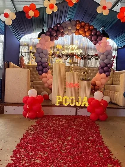 A grand party setup with a balloon arch and a red rose petal carpet runner.
