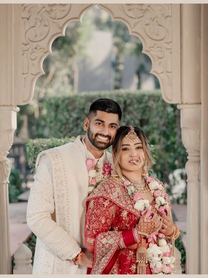 A happy portrait of the couple after their wedding ceremony. Framed by a beautiful archway, their garlands and joyful smiles capture the essence of the celebration.