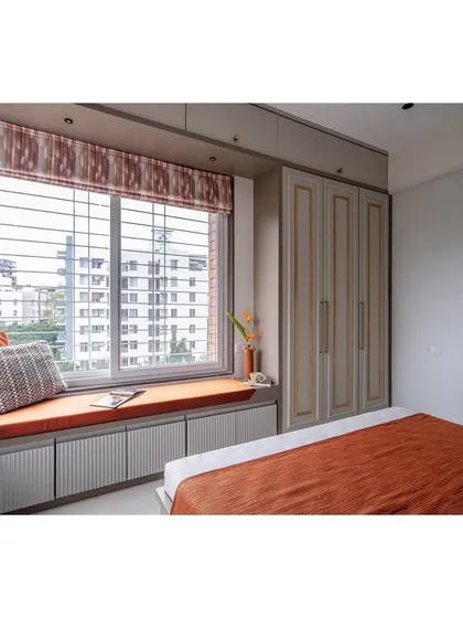 This view highlights the window seat, a perfect spot for reading and enjoying the city view. The custom wardrobes feature a classic design with elegant gold trim.