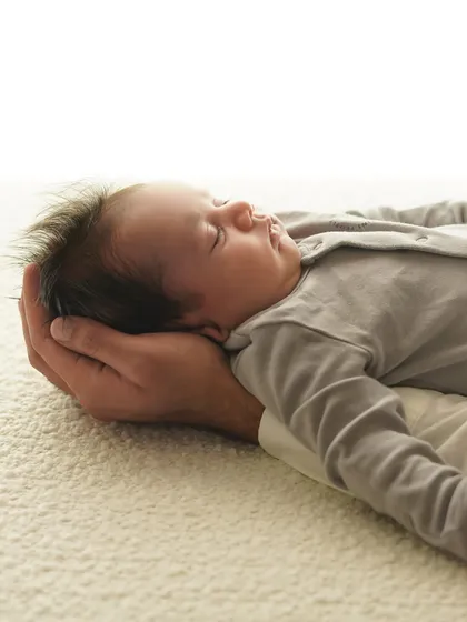 A parent's hand gently supports their newborn's head. This shot beautifully illustrates the scale of how small they are, and how much they are loved.