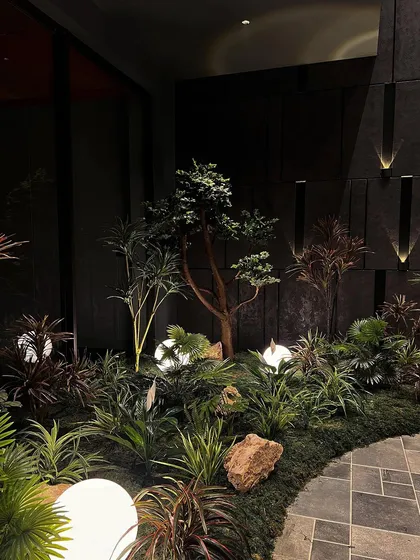 A nighttime view of the indoor garden, where uplighting on the dark wall panels adds another layer of dimension. The entire scene is designed to be a captivating visual experience.