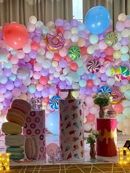 A 'sweet treats' themed party with a wall of pastel balloons. The setup includes donut and candy foil balloons, and pedestals decorated to look like ice cream cones and macarons.