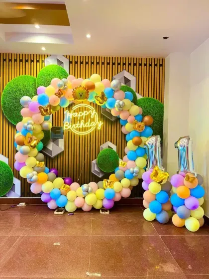 We create modern and vibrant first birthday decorations like this one. The setup features a colorful, asymmetrical balloon hoop, a custom 'Happy Birthday' neon sign for a trendy touch, and large '1' foil balloons to mark the special milestone. This style is perfect for a lively and stylish party.