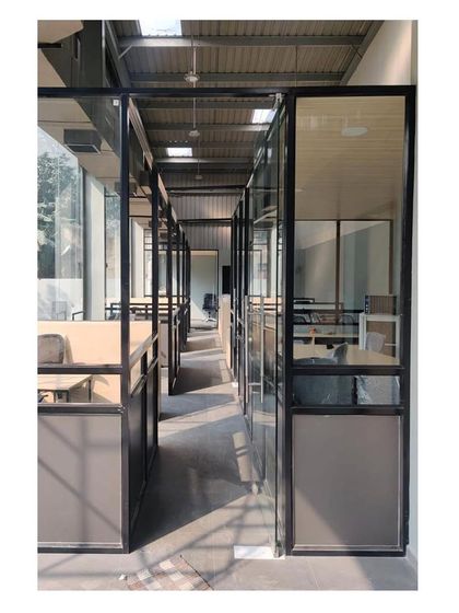 The main office corridor, lined with glass-walled cabins. This open-plan approach allows natural light to flood the workspace and promotes a sense of transparency and connection among the team.