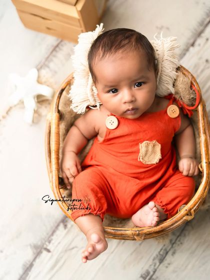 A curious three-month-old in a cute orange romper, sitting in a basket. We adapt our setups for older babies too.
