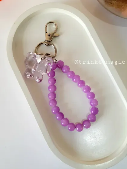 A single purple beaded bag charm with a matching translucent butterfly. The monochrome look is chic and trendy.