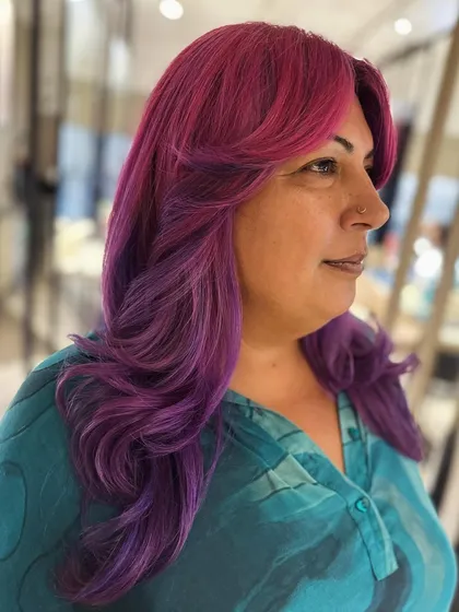 A fun and vibrant look with curtain bangs and face-framing layers. The pink and violet hair color makes a bold statement, and the cut adds beautiful shape.