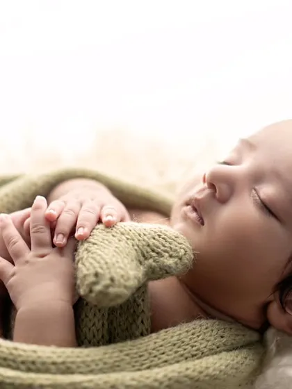 Holding a tiny heart. This newborn, wrapped in a soft green knit, is a beautiful symbol of new love and life.