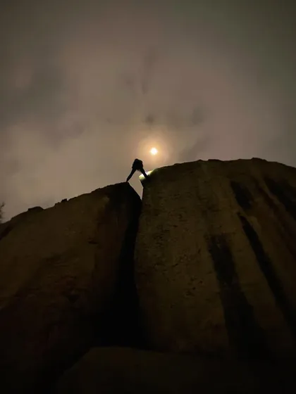 A climber tops out on a boulder, silhouetted against the full moon. Night climbing offers a unique perspective and a sense of quiet focus.