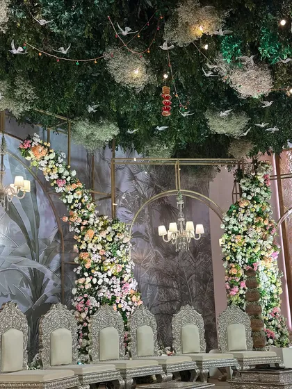 The main stage of the vintage garden wedding. A ceiling of lush greenery and hanging birds creates a canopy over the elegant silver thrones, making it feel like an enchanted forest.