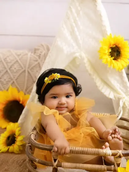 This six-month-old is sitting up in her basket, surrounded by sunflowers and a cute teepee backdrop.
