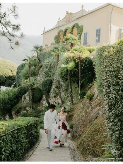 A couple walks down a garden path at an Italian villa on Lake Como. The lush greenery and classic architecture provide a stunning and romantic setting for their pre-wedding shoot.