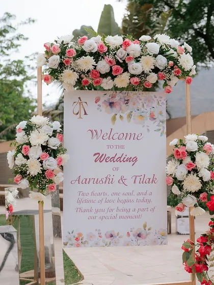 A soft and romantic welcome sign for a wedding, featuring a watercolor design and beautiful arrangements of pink and white roses.