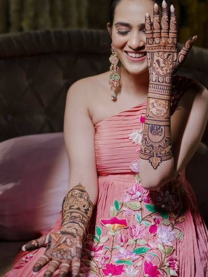 A joyful bride showing off her full-arm mehandi, her smile as bright as her henna.