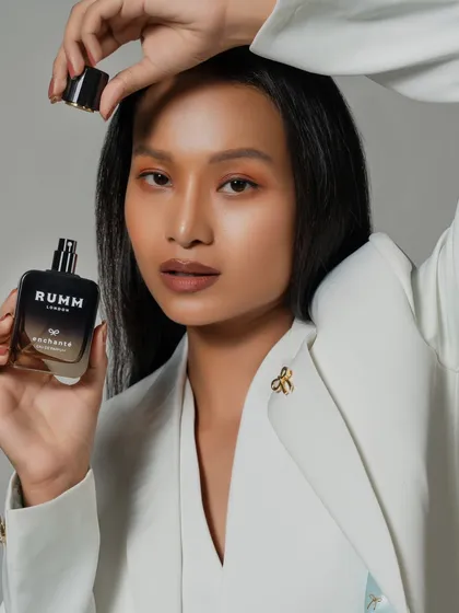 A clean and elegant shot for a perfume brand. The model's pose draws the eye to the bottle, presenting the fragrance as a key part of her sophisticated look.