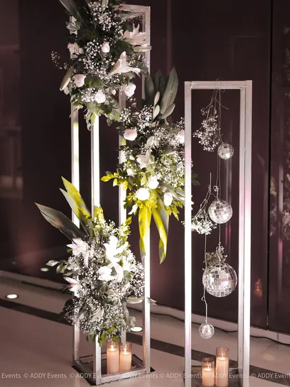 A modern and minimalist decor element, featuring white floral arrangements and hanging disco balls within sleek metallic frames.