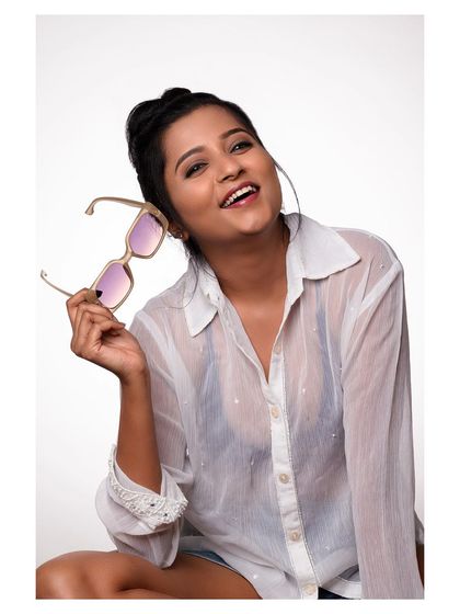 A fun and happy portrait of a model in a sheer white shirt and sunglasses. Her bright smile is infectious, creating a joyful and lighthearted image.
