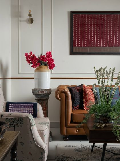 This room tells stories through textures and traditions. A classic tan chesterfield sofa is paired with a framed handloom textile, while a rustic pedestal holds a traditional bharani jar. These layered details create a living room that feels lived-in, loved, and beautifully rooted.