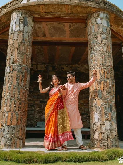 A fun, posed shot of the couple striking a dance pose within a stone gazebo at their Udaipur wedding venue.