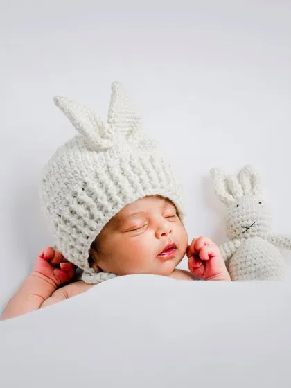 We love creating these adorable themed portraits. This sleeping baby in our hand-knitted bunny hat, complete with a matching toy, is one of our most requested newborn photoshoot setups.