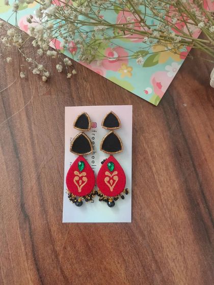 These two-part hand-painted earrings feature a black triangular stud and a red teardrop piece with a heart motif. The small black bead details add a delicate finishing touch.