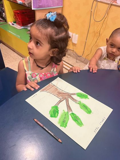 Her expression says it all. She's just finished her family tree handprint art and is watching her friends, completely engaged in the creative atmosphere of the classroom.