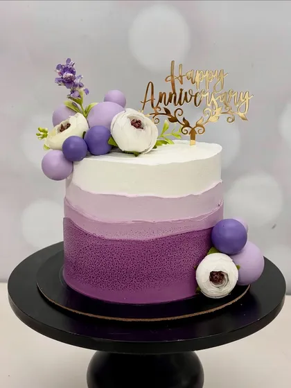 This anniversary cake features a stunning purple ombre design, decorated with purple spheres and delicate white and purple flowers. It's a cake that shows up dressed better than you!