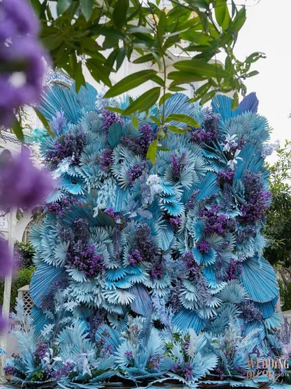 A dense, textural floral wall created with painted dried palms and flowers in shades of blue and purple. This served as a stunning, artistic photo backdrop.