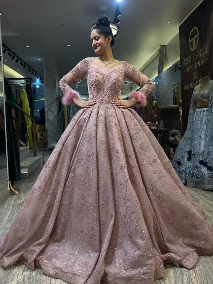 A full view of our glittery dusty pink Cinderella ball gown. The long sleeves with feather cuffs, fitted bodice, and voluminous skirt create a balanced and elegant silhouette. It’s a perfect choice for a winter engagement or reception.