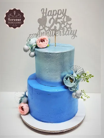 A striking 25th-anniversary cake in a silver and blue theme. This two-tier chocolate truffle cake is decorated with a metallic sheen and delicate flowers, perfect for celebrating a silver jubilee.