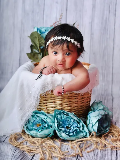 A wider view of the baby in the basket, showing the surrounding blue flowers and rustic jute details that complete the scene.