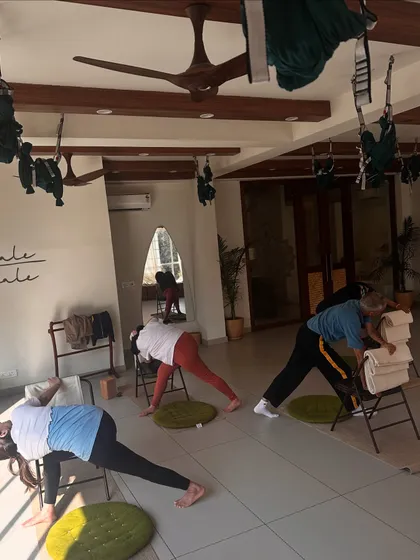 A chair yoga class in session, with students using chairs to modify a standing forward bend, making it accessible for all.