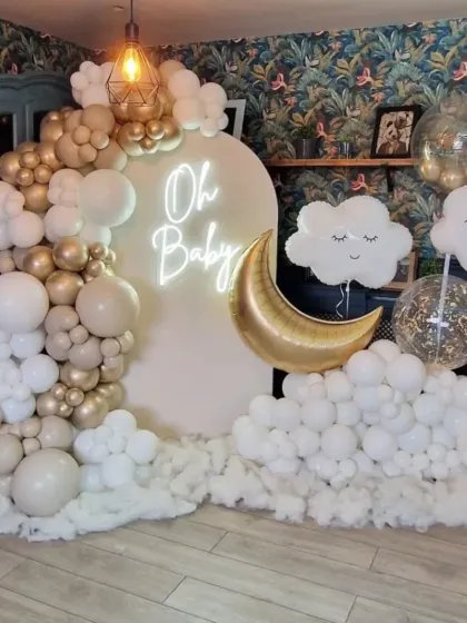 A dreamy 'Oh Baby' baby shower theme with a moon and clouds motif. The decor uses a neutral color palette with gold accents and a soft neon sign.
