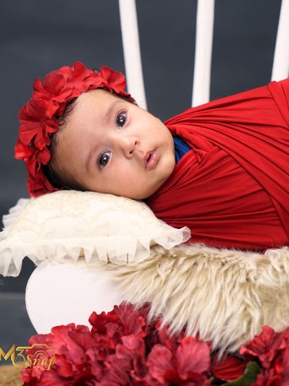 A close-up portrait of the baby girl with a red floral headband. Her big, curious eyes are just mesmerizing.