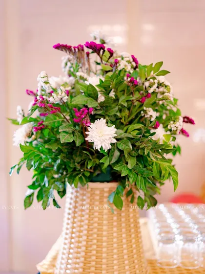 A rustic floral arrangement in a woven basket, combining white chrysanthemums and purple statice for a touch of earthy elegance.