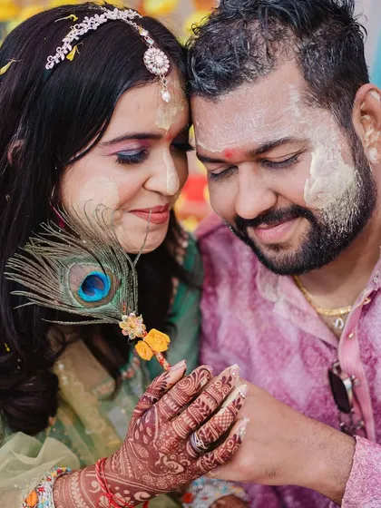 An intimate close-up of the couple during their Haldi, sharing a quiet moment amidst the fun, with a peacock feather adding a traditional touch.