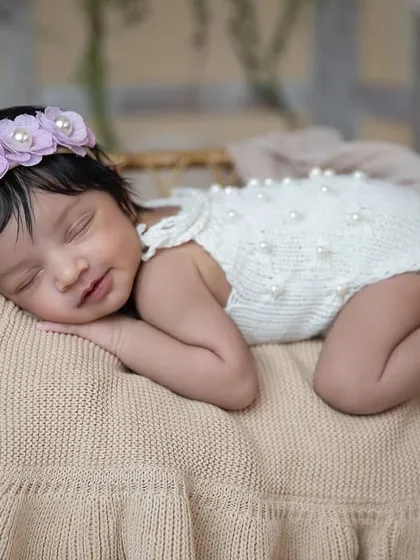 This peaceful portrait captures a newborn girl in a beautiful white knit outfit, sleeping soundly on a soft blanket. It only takes nine months to create a lifetime of love.