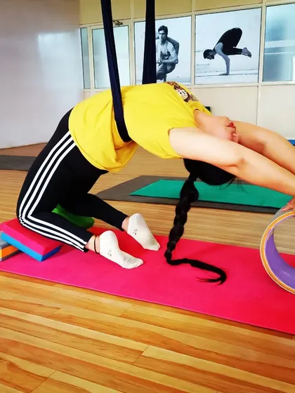 I am assisting a student in a deep backbend, using both an aerial hammock and a yoga wheel. This combination of props allows for maximum support and opening.