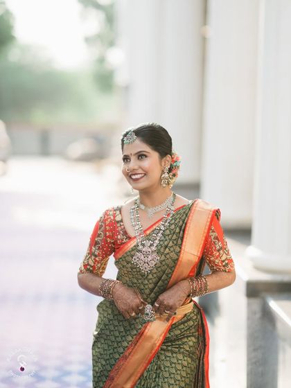 A happy bride in a traditional green saree, posing against white pillars.