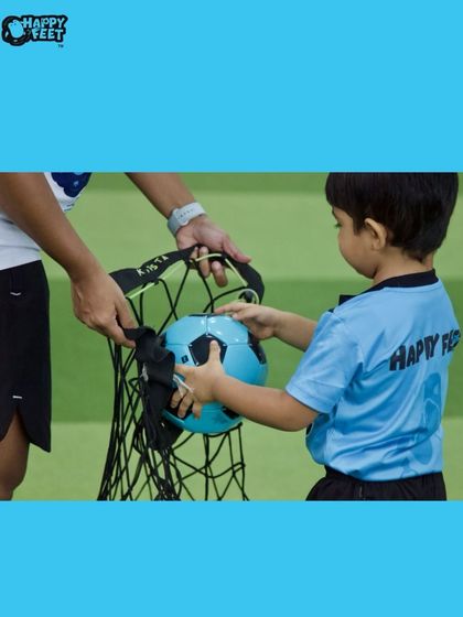 Teamwork makes the dream work, even when it comes to packing up! A child helps a coach put a football into the bag, learning about responsibility and helping out after a fun session.