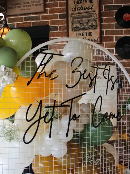 This custom backdrop with the message 'The Best Is Yet To Come' was a centerpiece for a lemon-themed baby shower. The mesh arch with a cascade of green, yellow, and white balloons created a modern and cheerful photo opportunity.