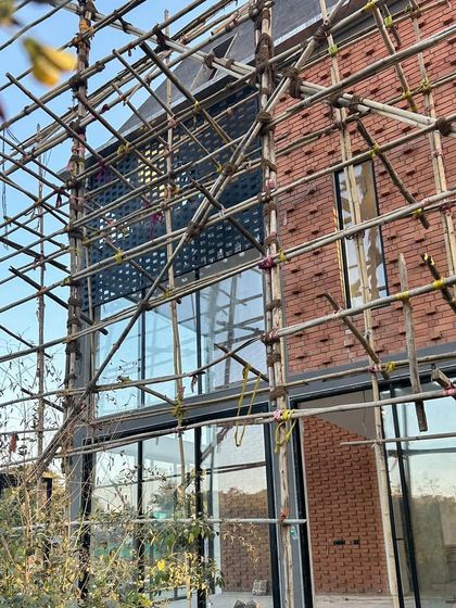 The facade of a home in our Kolgaon Masterplan, seen here during construction. The image shows the patchwork of brick and glass taking shape, with scaffolding revealing the layers of craftsmanship involved in creating the perforated screens.