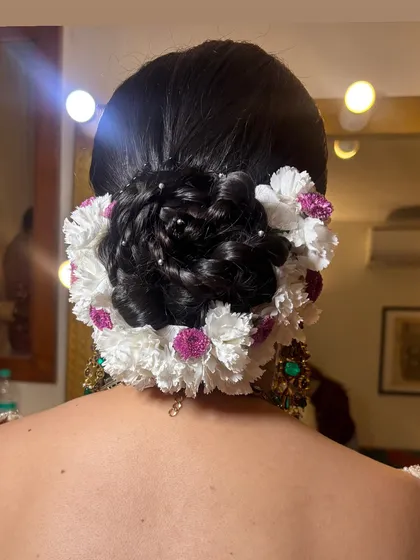 A detailed close-up of a floral bridal bun. I created an intricate braided pattern within the bun itself and then decorated it with a mix of white and purple flowers and tiny pearls for a delicate, multi-dimensional effect.