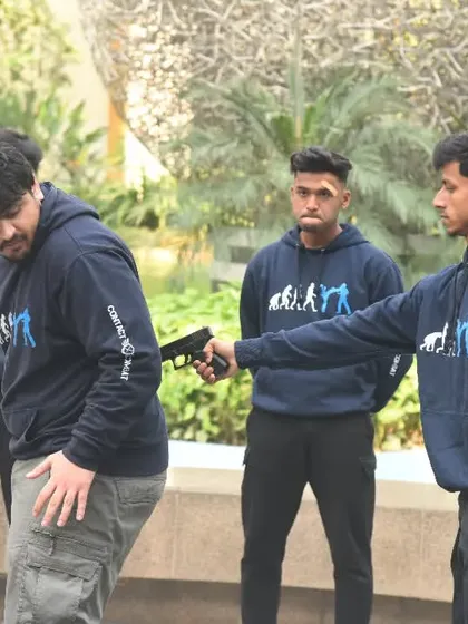 A gun to your back is a worst-case scenario, and I train you for it. This image shows a gun defense drill, focusing on how to turn, redirect the weapon away from your body, and gain control when you have no other choice.