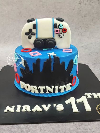 A Fortnite cake for an 11th birthday, featuring a handcrafted, edible game controller on top of a blue cake with a city skyline design.