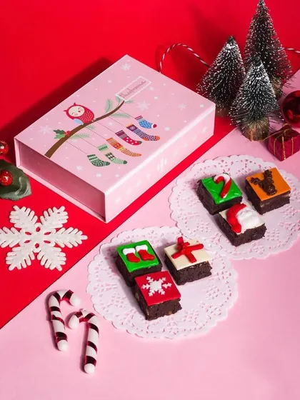 A sweet and simple flatlay of a pink Christmas gift box with assorted brownies and candy canes. The two-tone background and clean arrangement give it a modern and cheerful holiday feel.