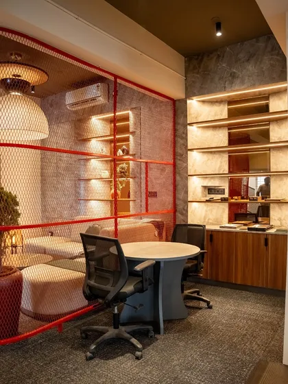 A sectional view showing the relationship between a discussion table and the adjacent lounge area. The red mesh partition creates a visual connection while maintaining a degree of separation between zones.