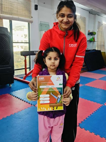 A very young gymnast proudly holds her "JUMP" certificate.